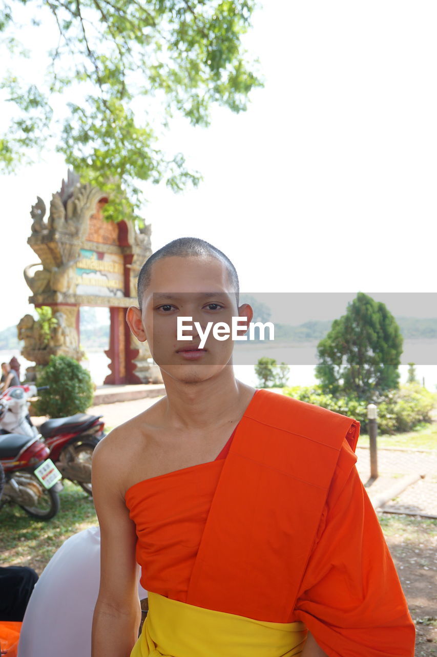 Portrait of monk standing against sky
