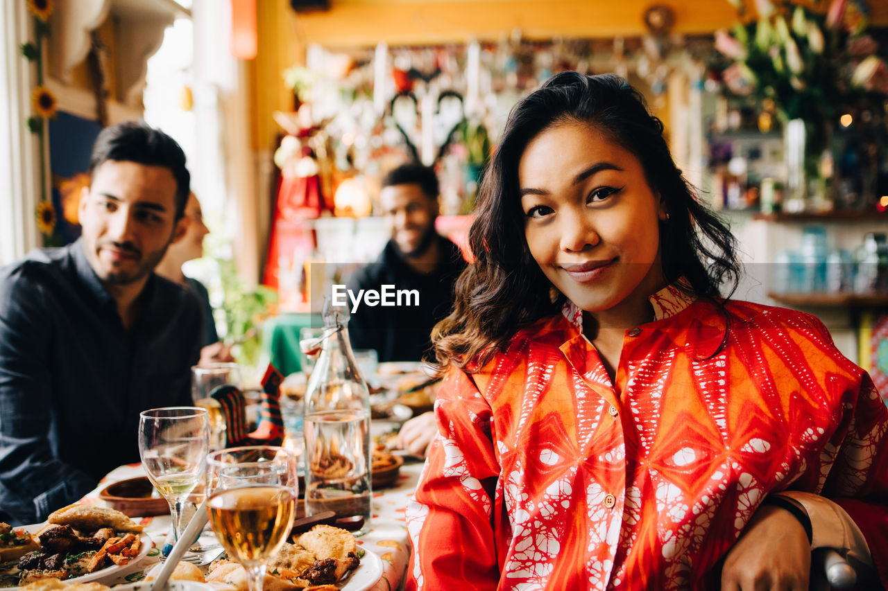 Portrait of smiling young woman sitting at table against multi-ethnic friends enjoying brunch in restaurant