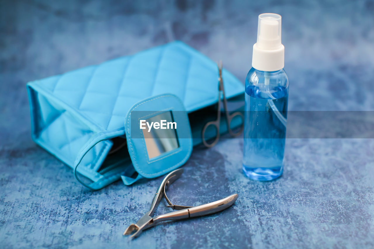 Close-up of small spray bottle with clutch bag and tweezers on blue table