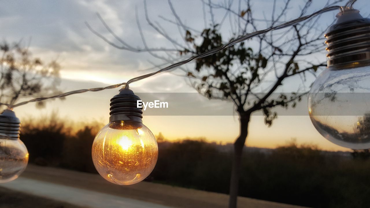 CLOSE-UP OF LIGHT BULB AGAINST SKY DURING SUNSET