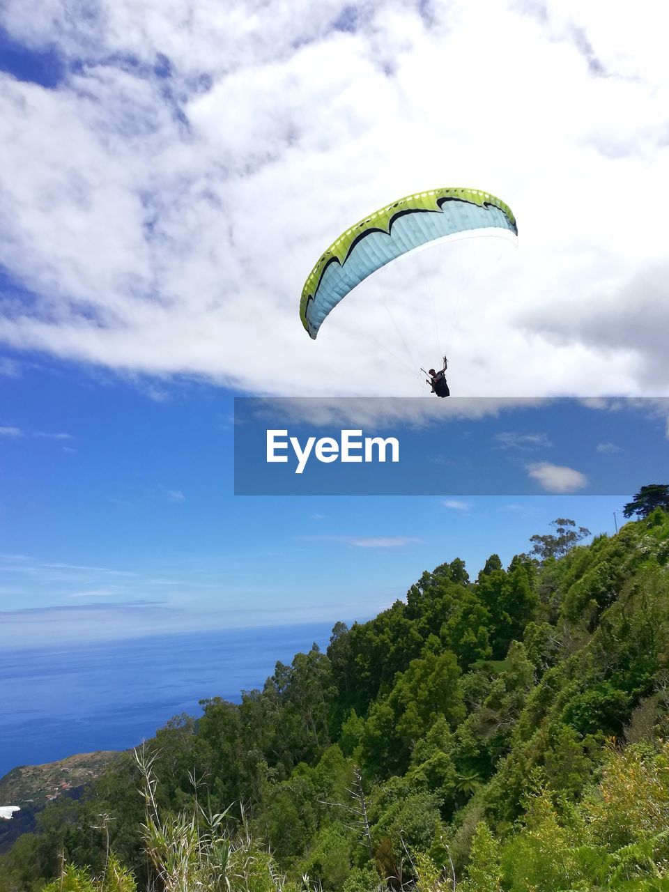 PERSON PARAGLIDING OVER GREEN LANDSCAPE AGAINST SKY