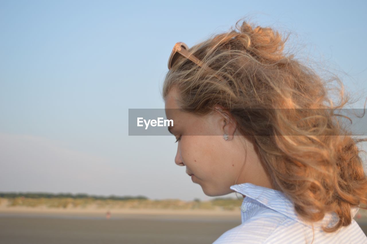 Close-up of teenage girl looking down against sky