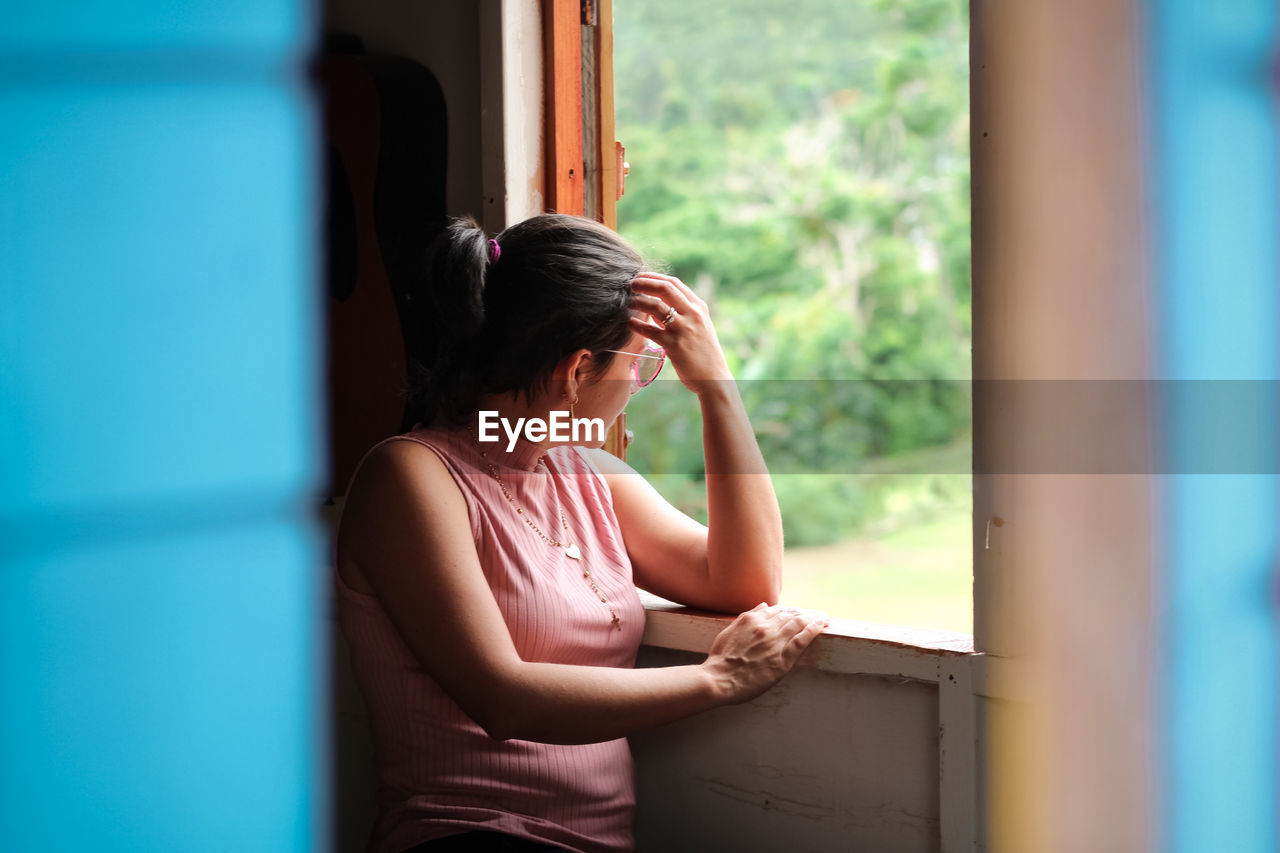 Woman looking away while sitting on window at home