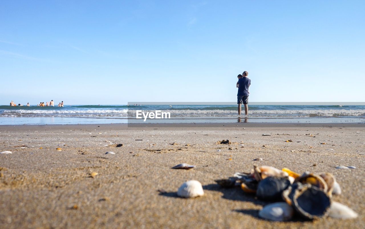 Rear view full length of father with baby boy on shore at beach against sky