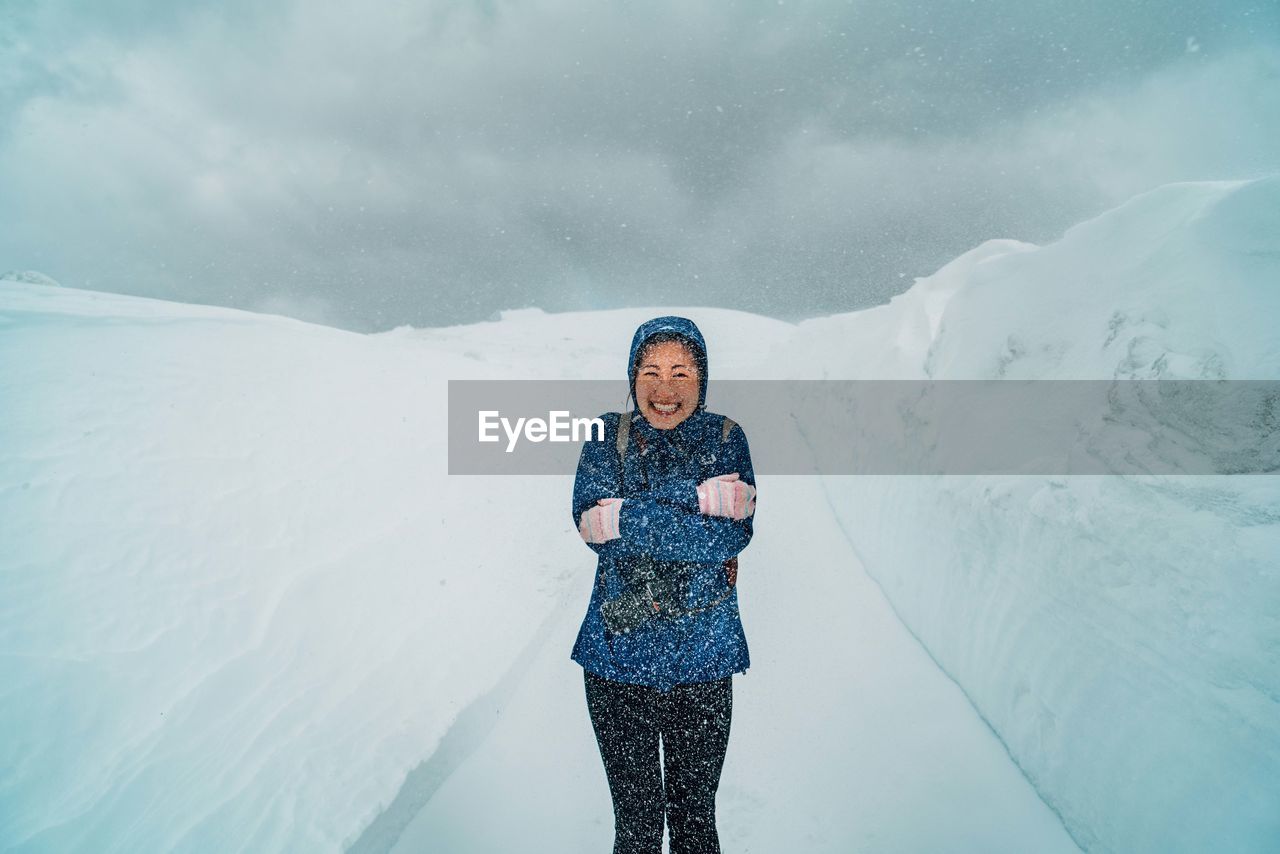 Portrait of smiling woman standing on mountain during snowfall