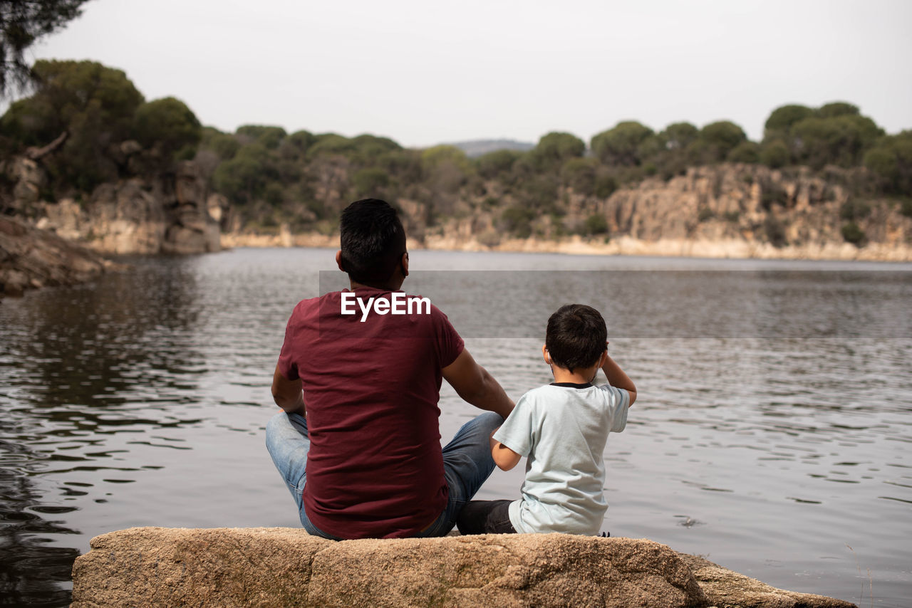 Rear view of father and son sitting on a wide riverside