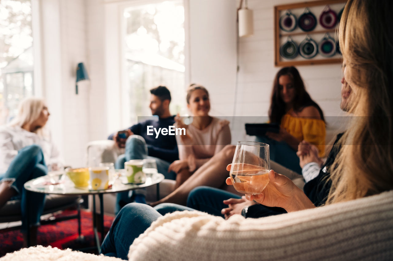 Woman holding glass while sitting with friends in cottage