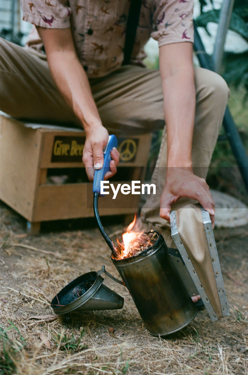 one person, adult, heat, holding, fire, flame, burning, men, nature, food and drink, blacksmith, spring, container, occupation, working, food, casual clothing, lifestyles, day, outdoors, person, standing, low section, domestic life
