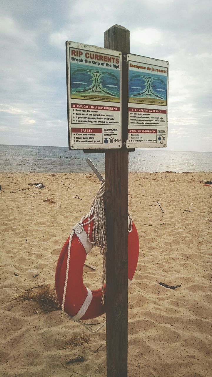 Life belt with ropes hanging on signboard on sandy beach