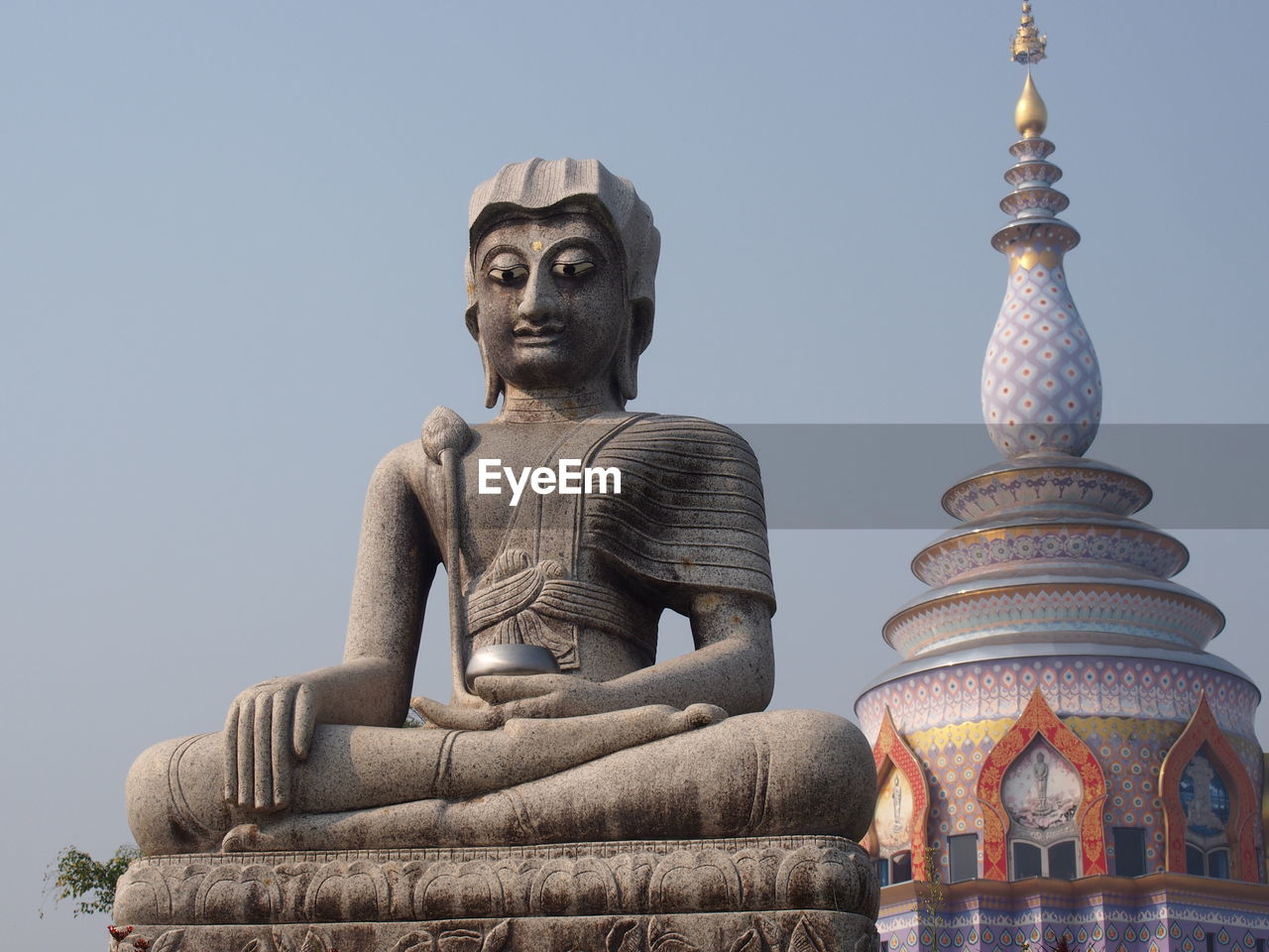 Low angle view of buddha statue by temple against clear sky
