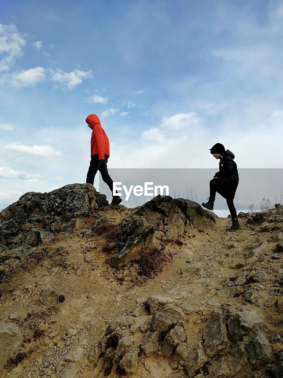 Two children walking on rocks against sky during autumn day