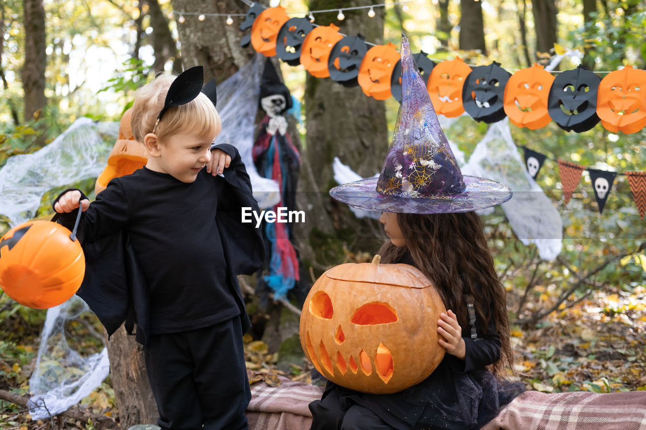 Two kids girl and boy in halloween costume with pumpkins in halloween decorations outdoor