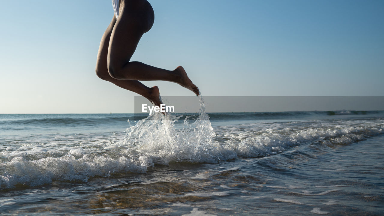 Side view anonymous black woman jumping on the beach