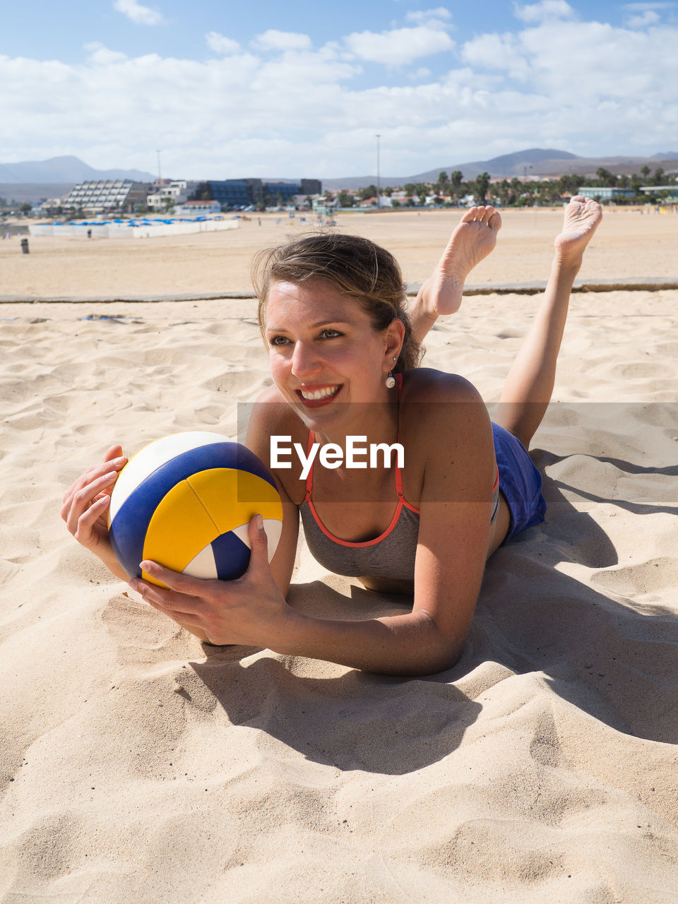 Woman lying with volleyball on sand at beach