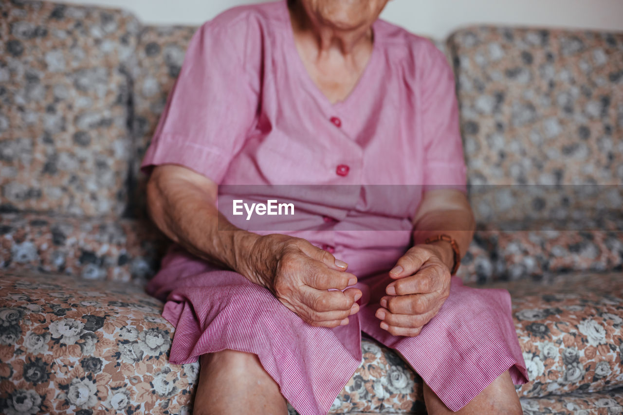 Front view of a unrecognizable senior woman with alzheimer's mental health issues sitting in a sofa alone in her home