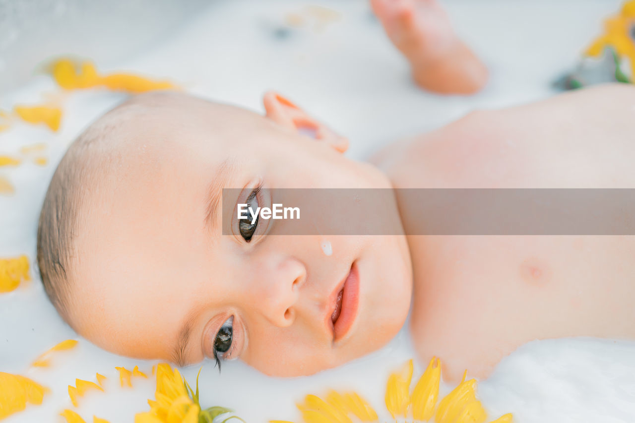 Portrait of cute baby lying on milk bath with flowers 