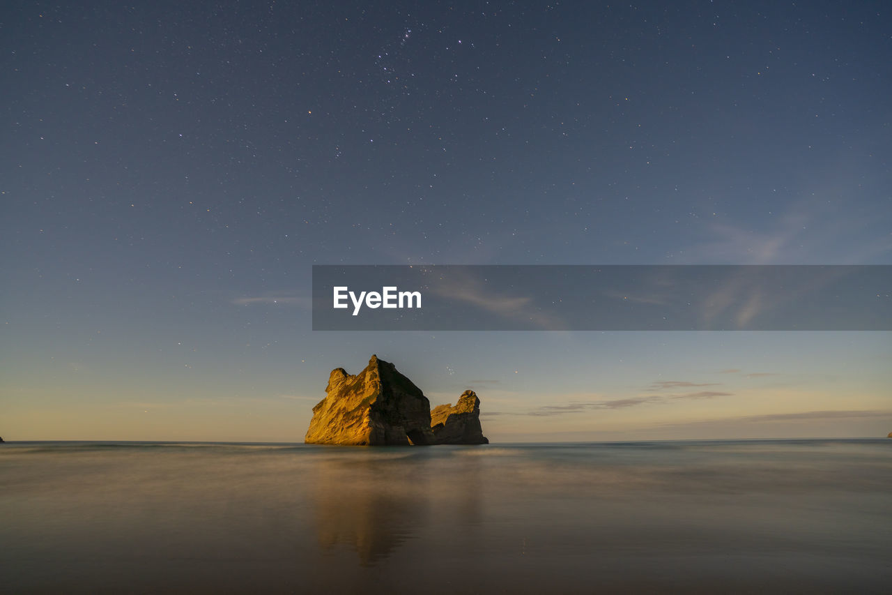 ROCK FORMATION IN SEA AGAINST SKY AT SUNSET