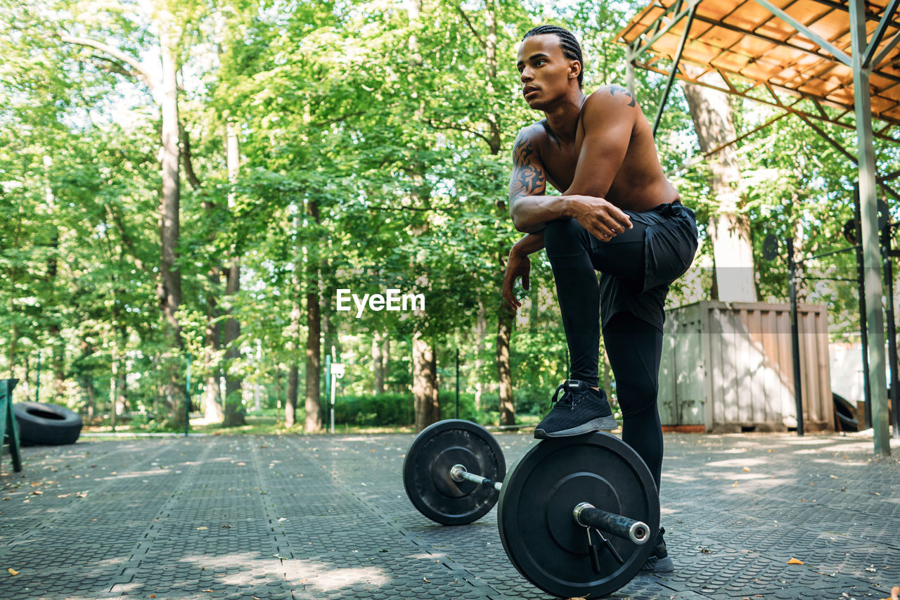 Young man looking away while standing with barbell