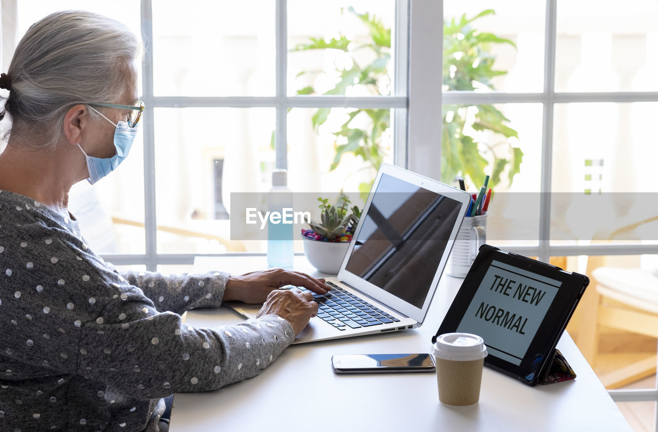 Senior woman wearing mask using laptop at home