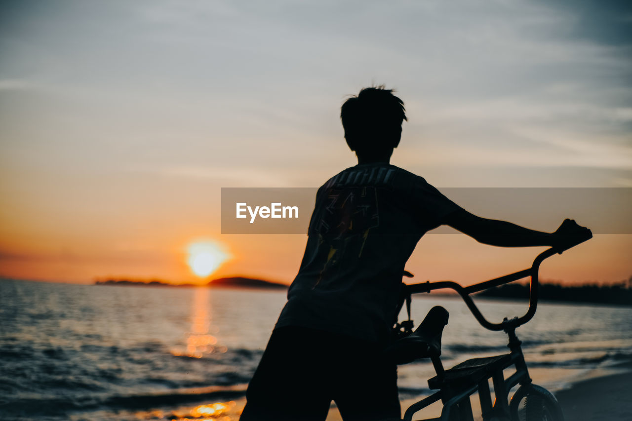 Silhouette man standing on beach against sky during sunset