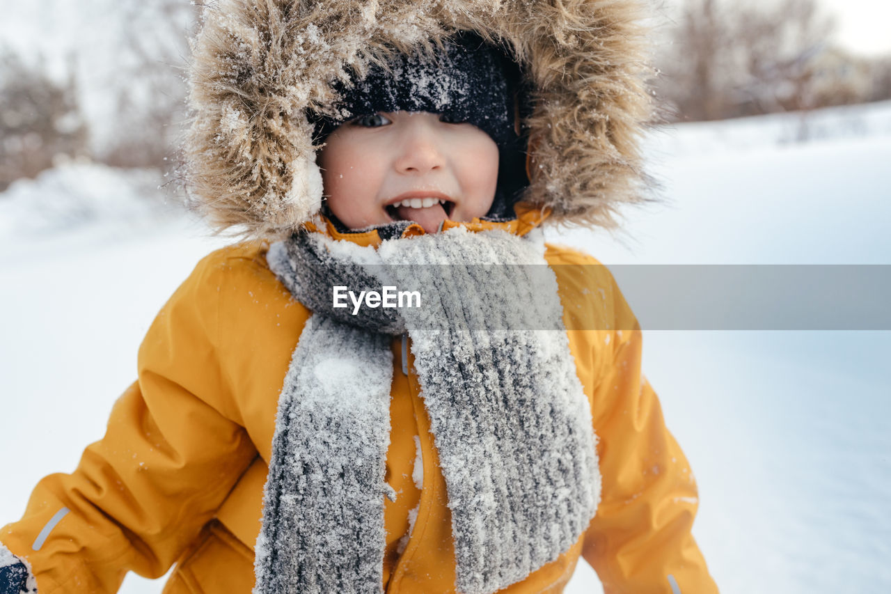 Smiling child in a fur hood in a knitted scarf and an orange winter jacket. outdoors. fashionable 