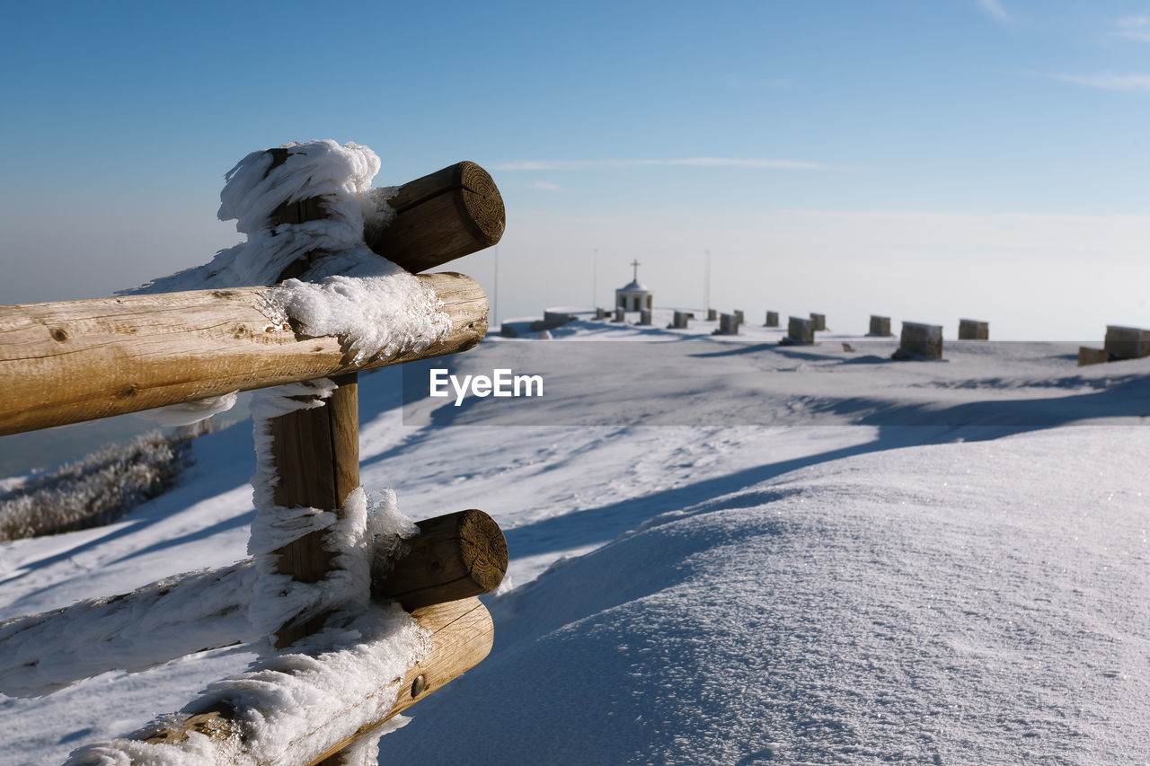 SNOW COVERED WOODEN POSTS ON BEACH AGAINST SKY