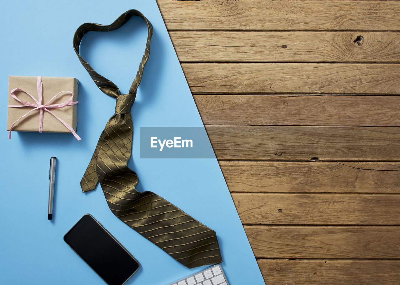 Close-up of necktie with mobile phone and gift on wooden table