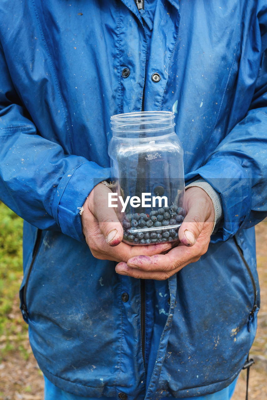 Hand of a picker holding a container with wild blueberries in the forest.