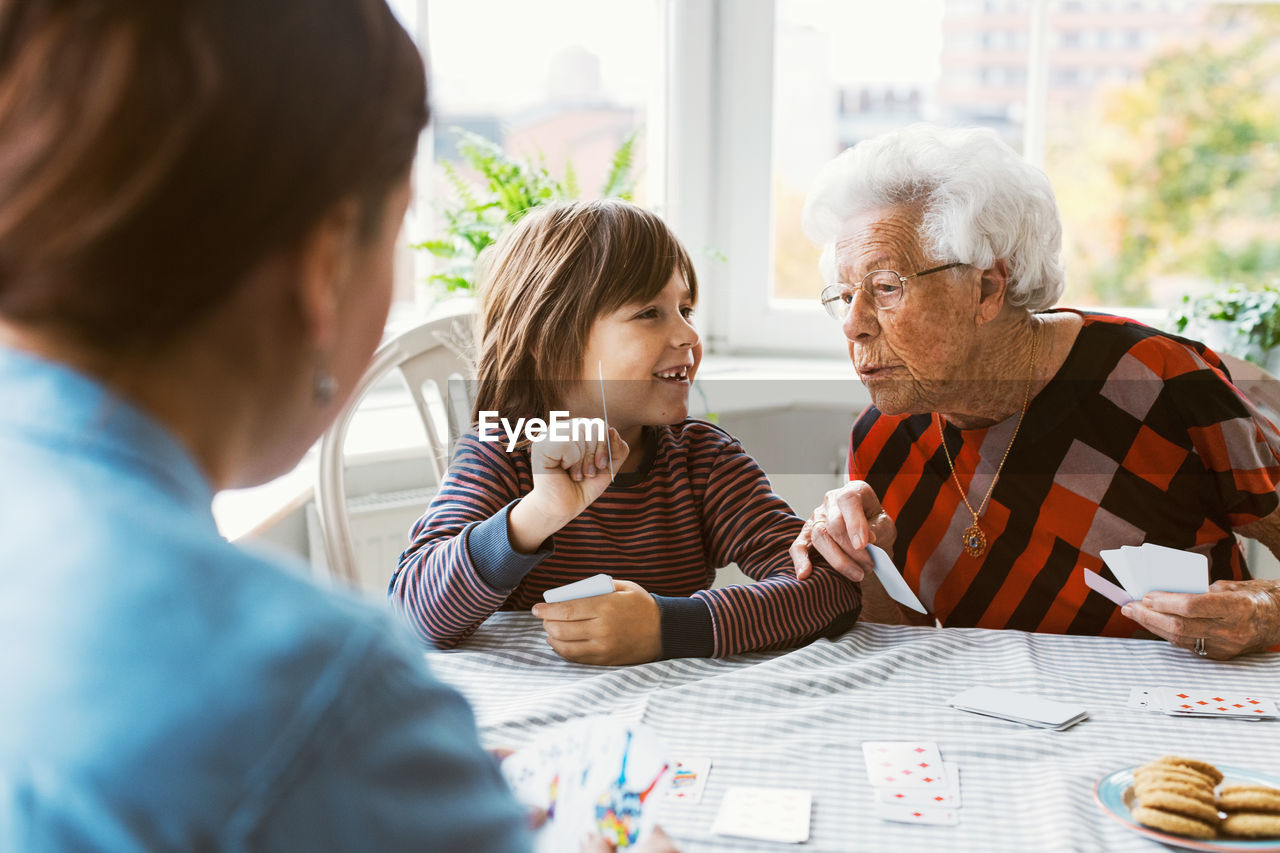 Happy boy showing playing card with great grandmother at home