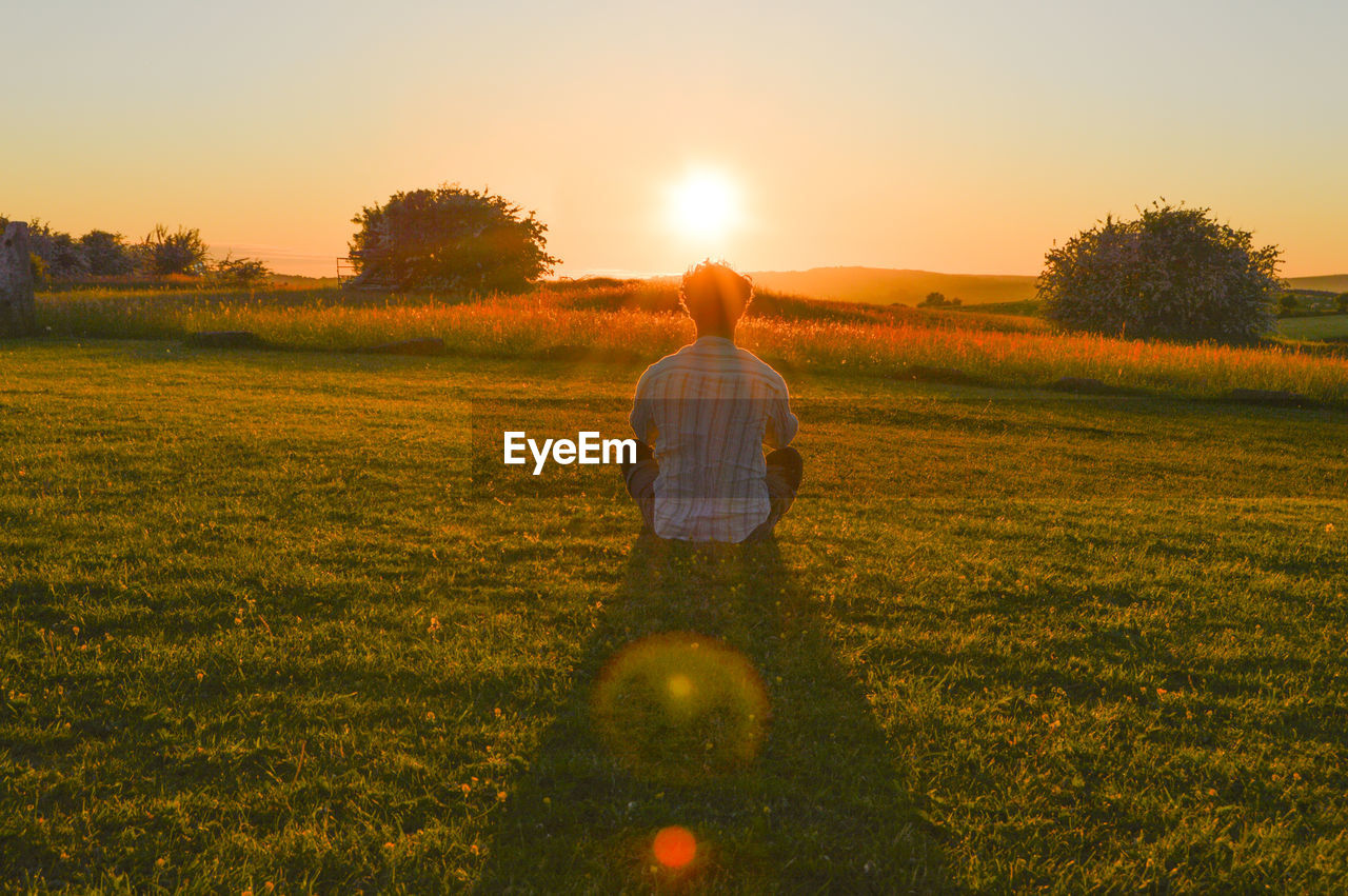 REAR VIEW OF MAN ON FIELD DURING SUNSET