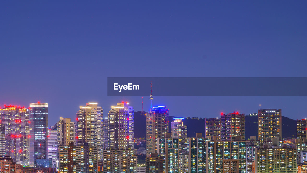 ILLUMINATED BUILDINGS AGAINST CLEAR BLUE SKY