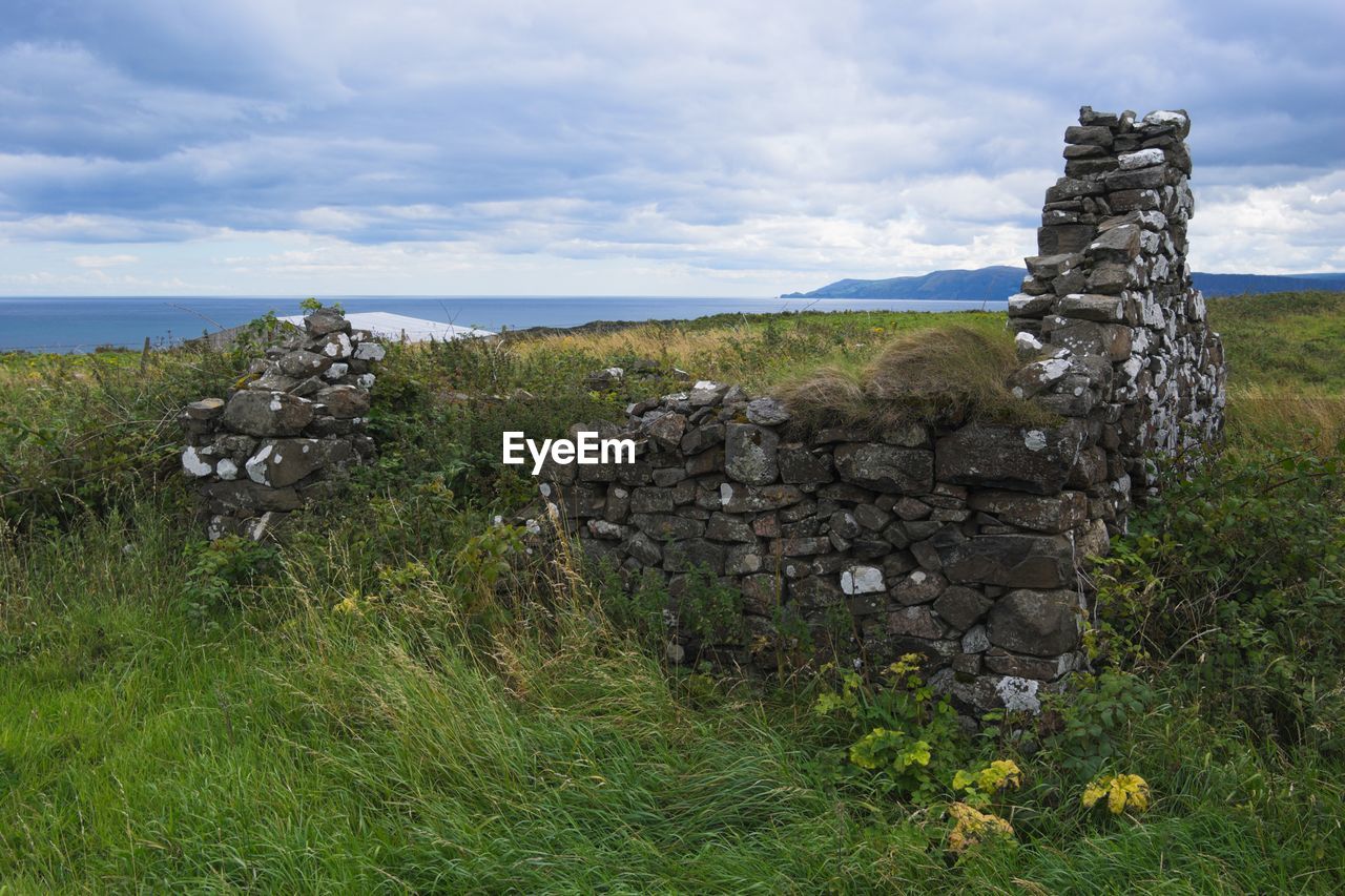 Old stone wall on grassy field against cloudy sky