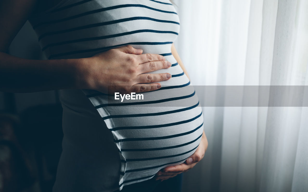 Midsection of pregnant woman standing at home