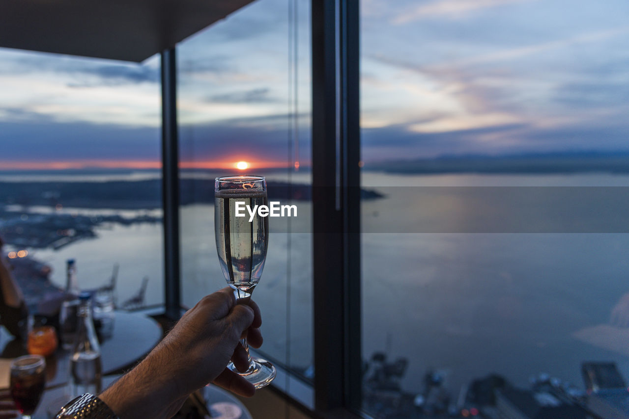 Cropped hand holding champagne flute in restaurant by sea