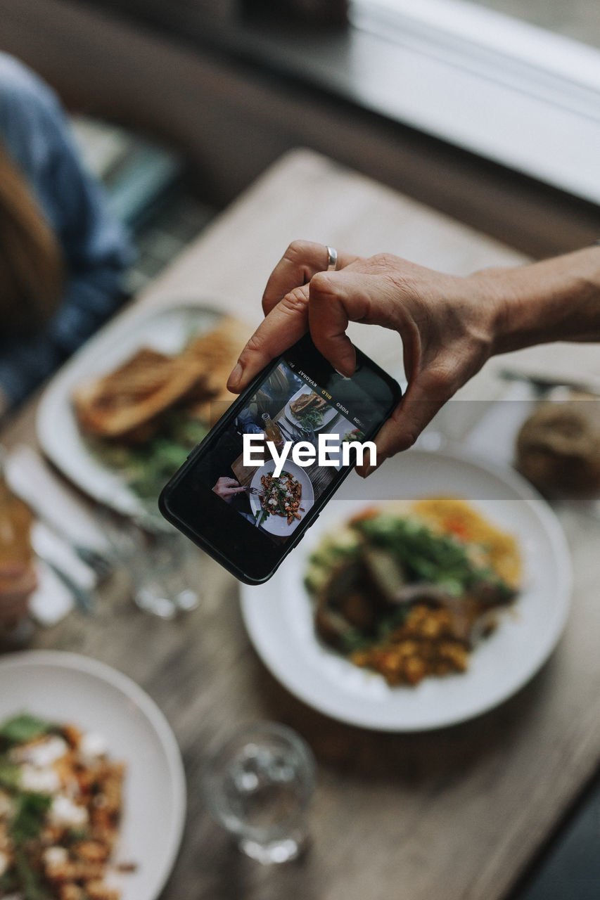 Hand with cell phone photographing food on table