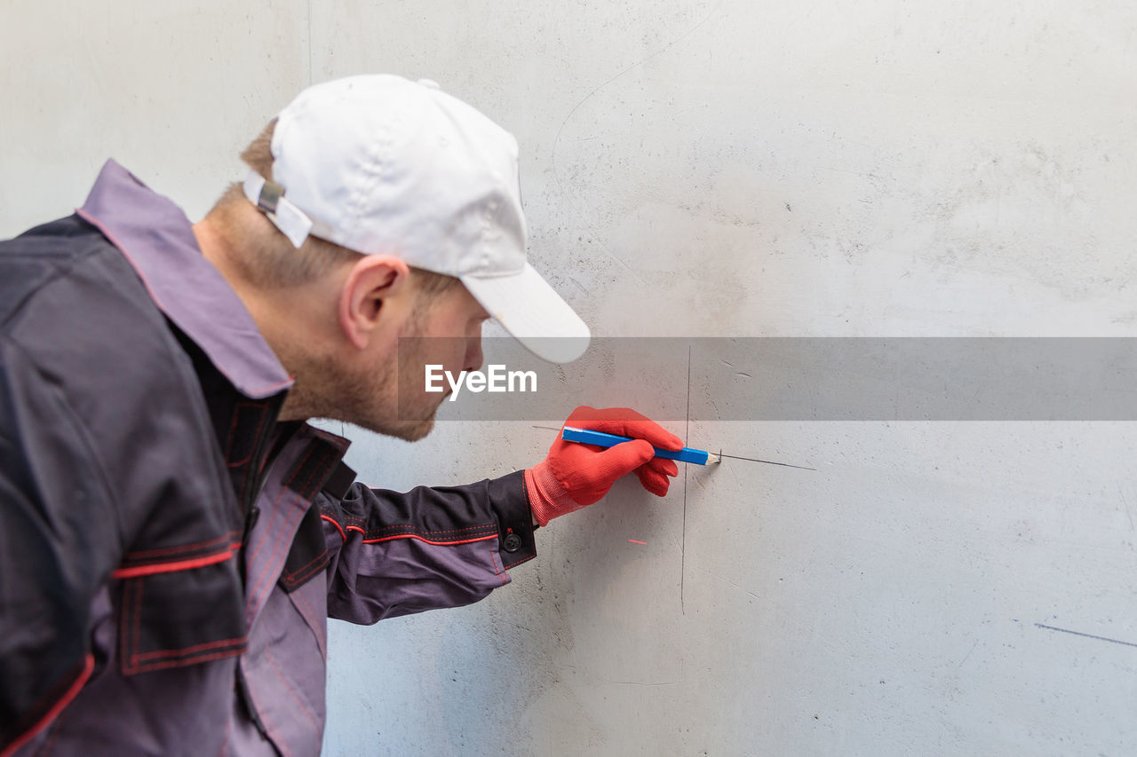 A man, an electrician marks out holes for sockets with a pencil, a tape measure