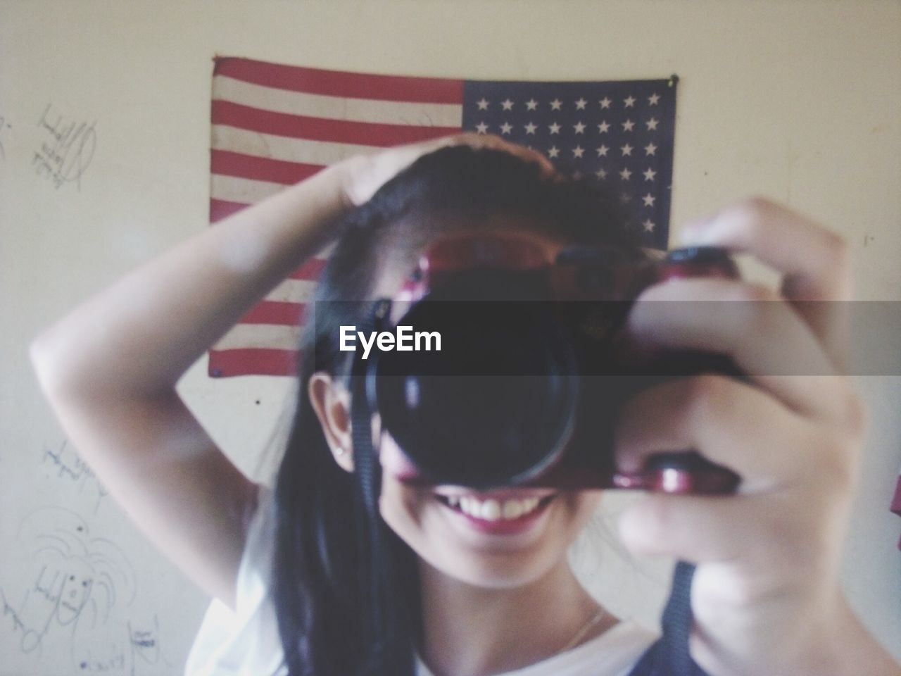 Happy girl holding digital camera in front of american flag