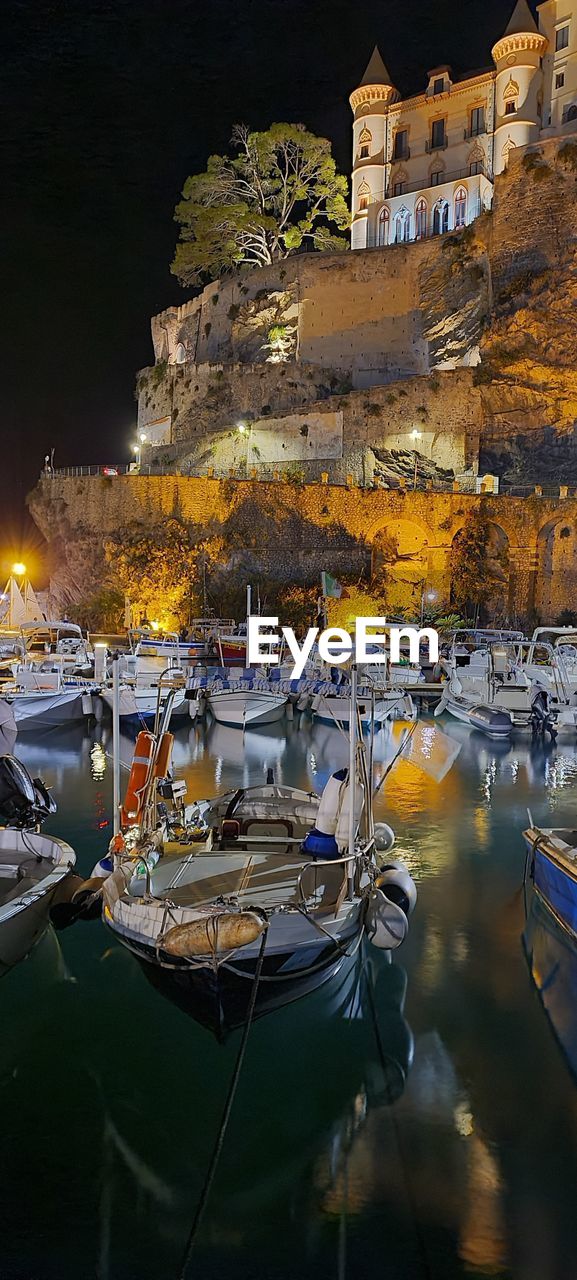 Boats moored at harbor by buildings in city at night