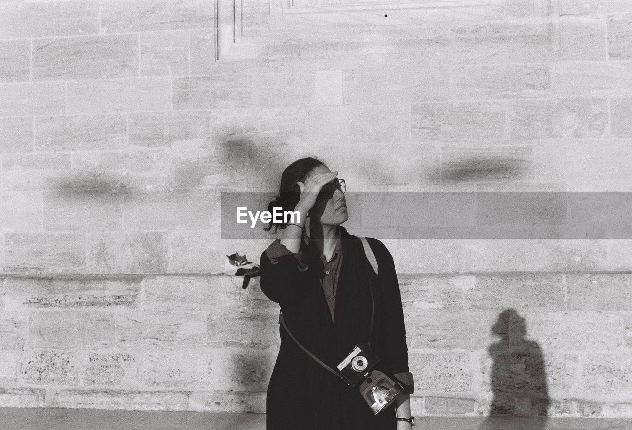 Woman shielding eyes while standing against wall