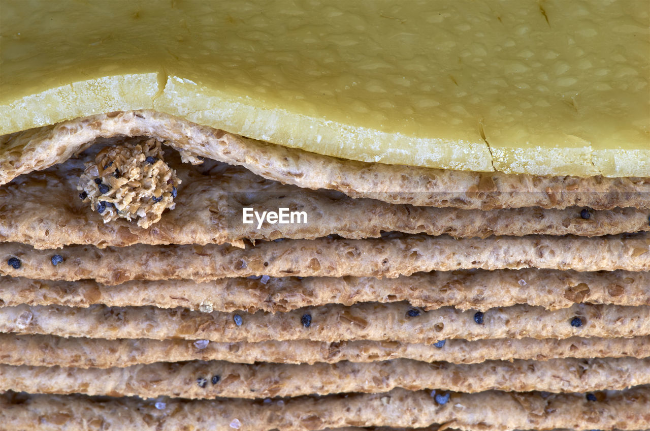 A rogue lump of crumbs, disrupts a uniform stack of multigrain crackers, with sweaty cheese on top.