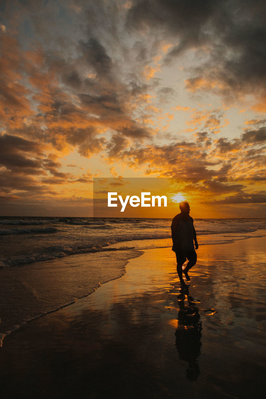 Silhouette man walking at beach against sky during sunset