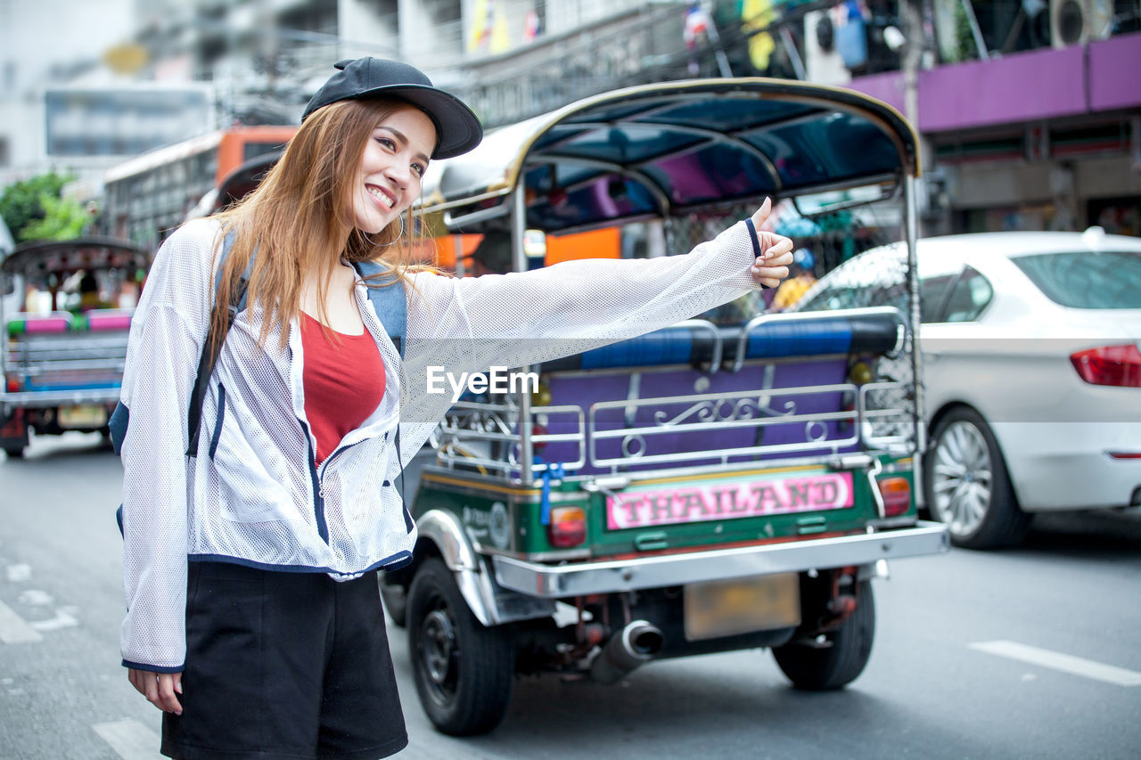 Smiling beautiful woman hitchhiking on city street against jinrikisha