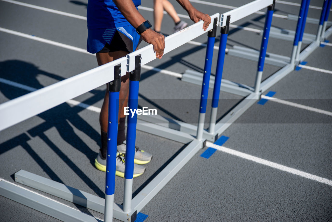 Young man positions hurdles lined up on running track