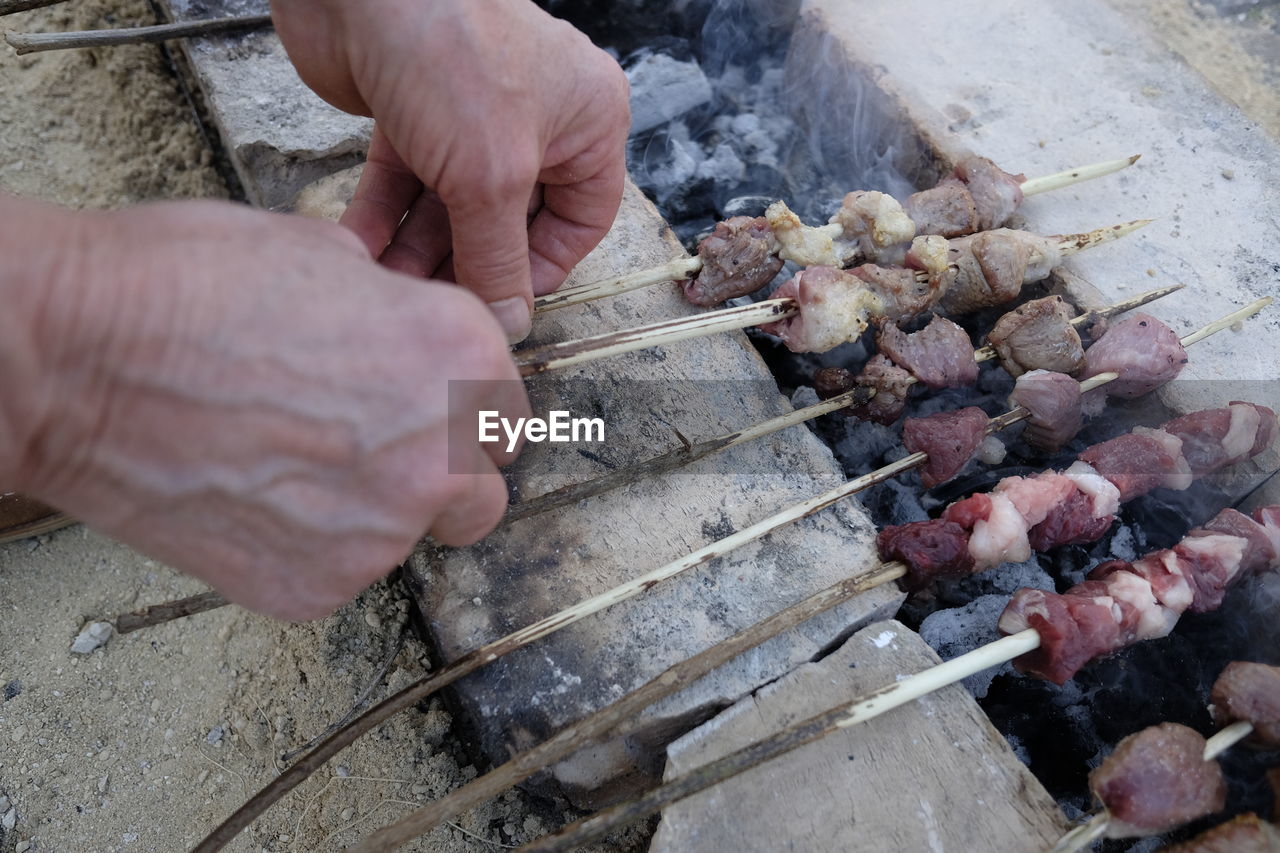 High angle view of man cooking meat skewers on barbecue