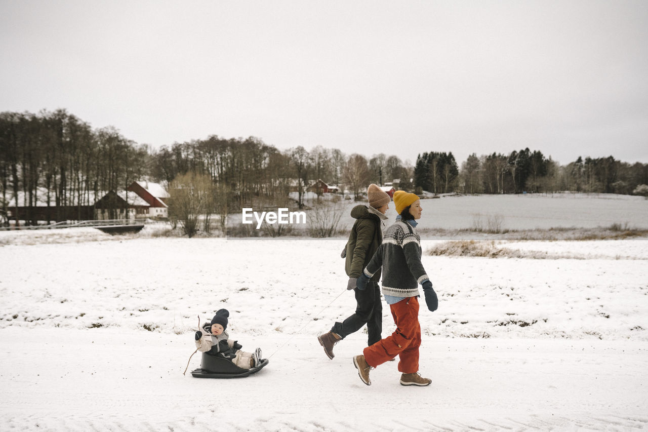 Full length of lesbian mothers pulling daughter while walking on snow