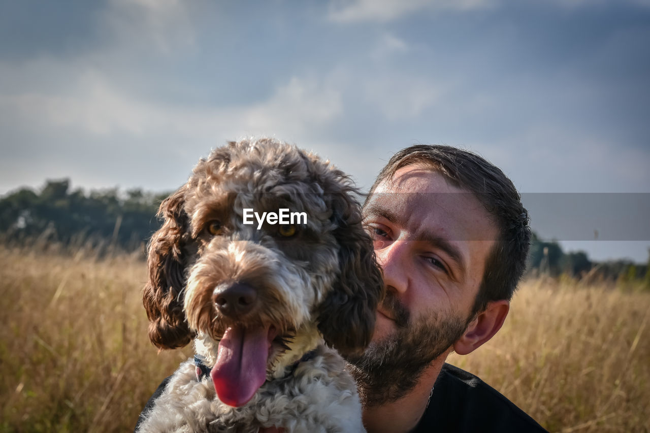Portrait of man and dog on field against sky