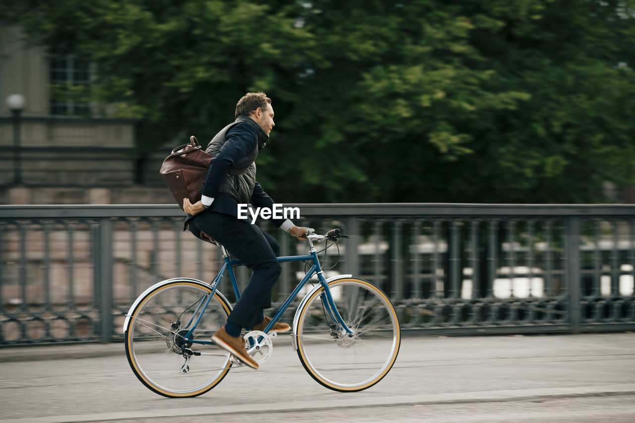 Side view of businessman with bag riding bicycle on bridge