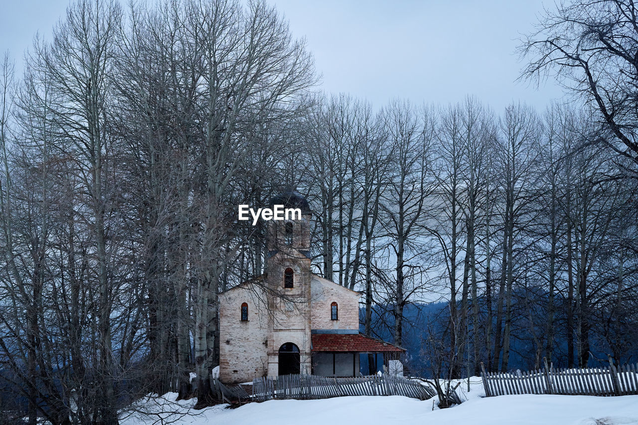 SNOW COVERED FIELD BY BUILDING AGAINST SKY