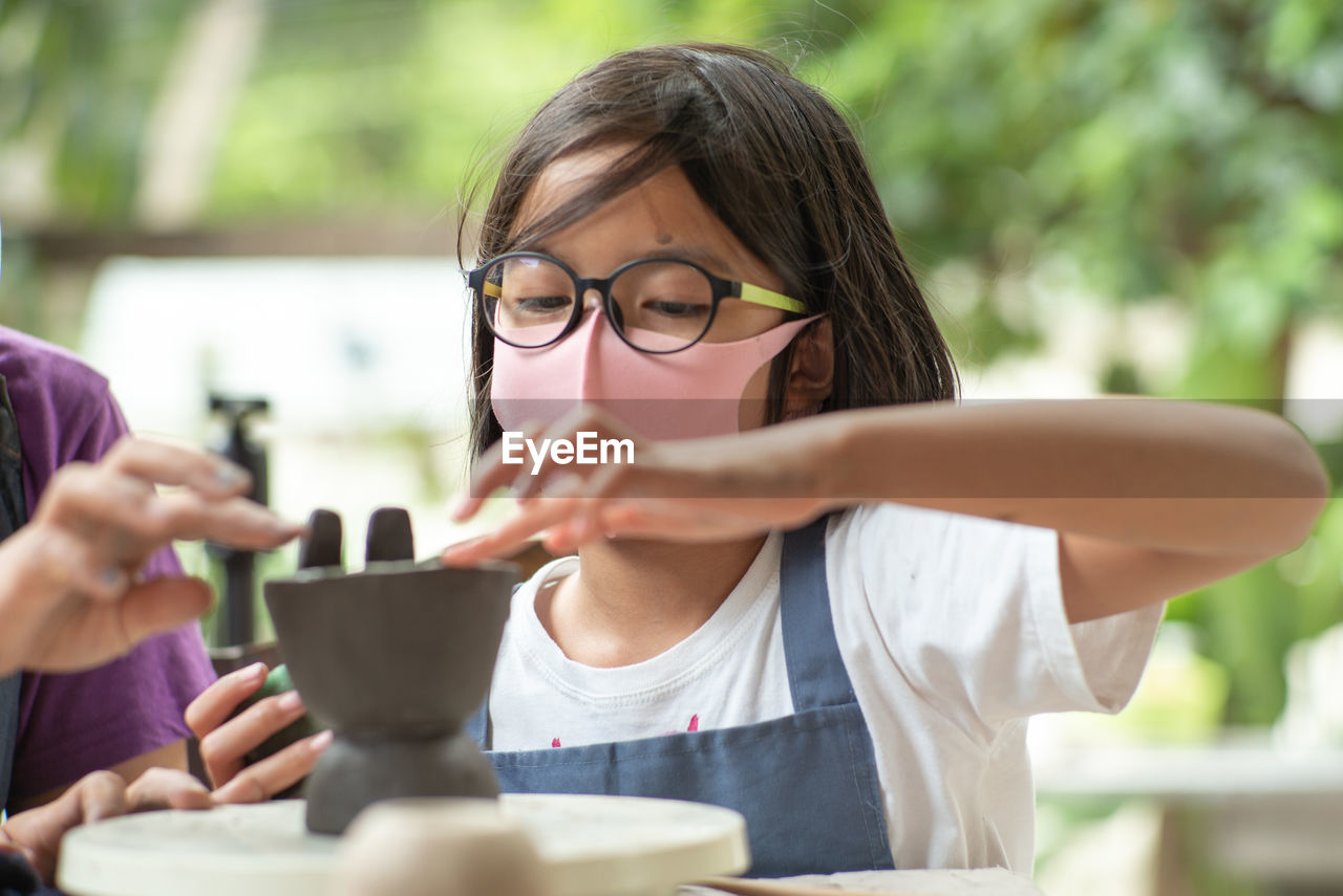 Closeup dirty face of asian girl with eyeglasses learns how to mold the clay work in workshop class