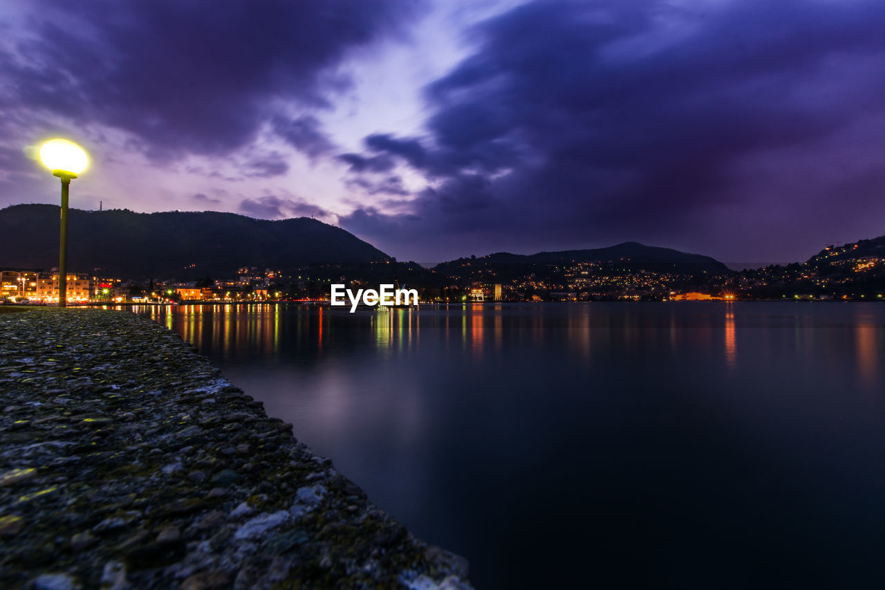 SCENIC VIEW OF ILLUMINATED LAKE AGAINST SKY AT DUSK